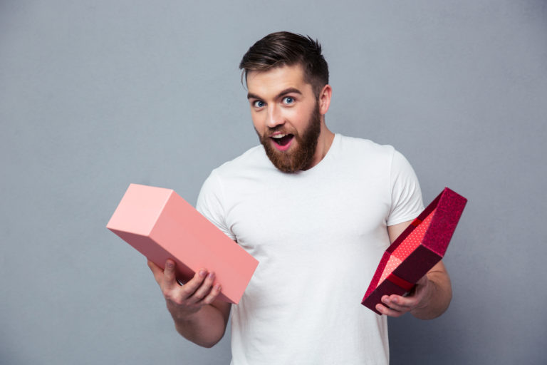 Portrait Of A Young Man Opening Gift Box Over Gray Background